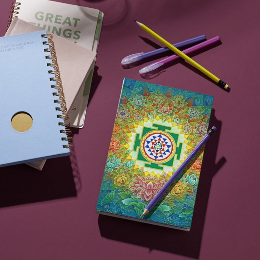 Sri Yantra Notebook with vibrant sacred geometry cover placed on a purple desk with pens and other notebooks, ideal for journaling and gifting.