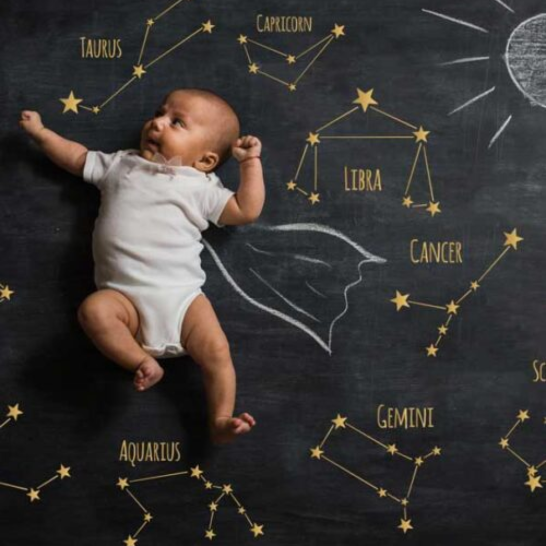 Infant lying on zodiac-themed chalkboard backdrop with constellations and astrological signs, symbolizing Santati Margdarshan for parenthood guidance.